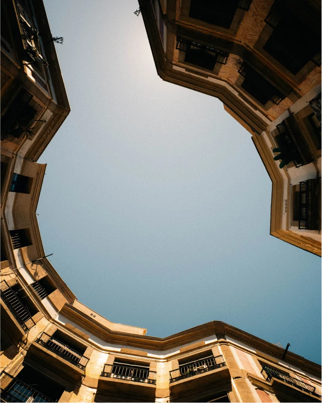 View upwards between warm stone buildings towards the sky