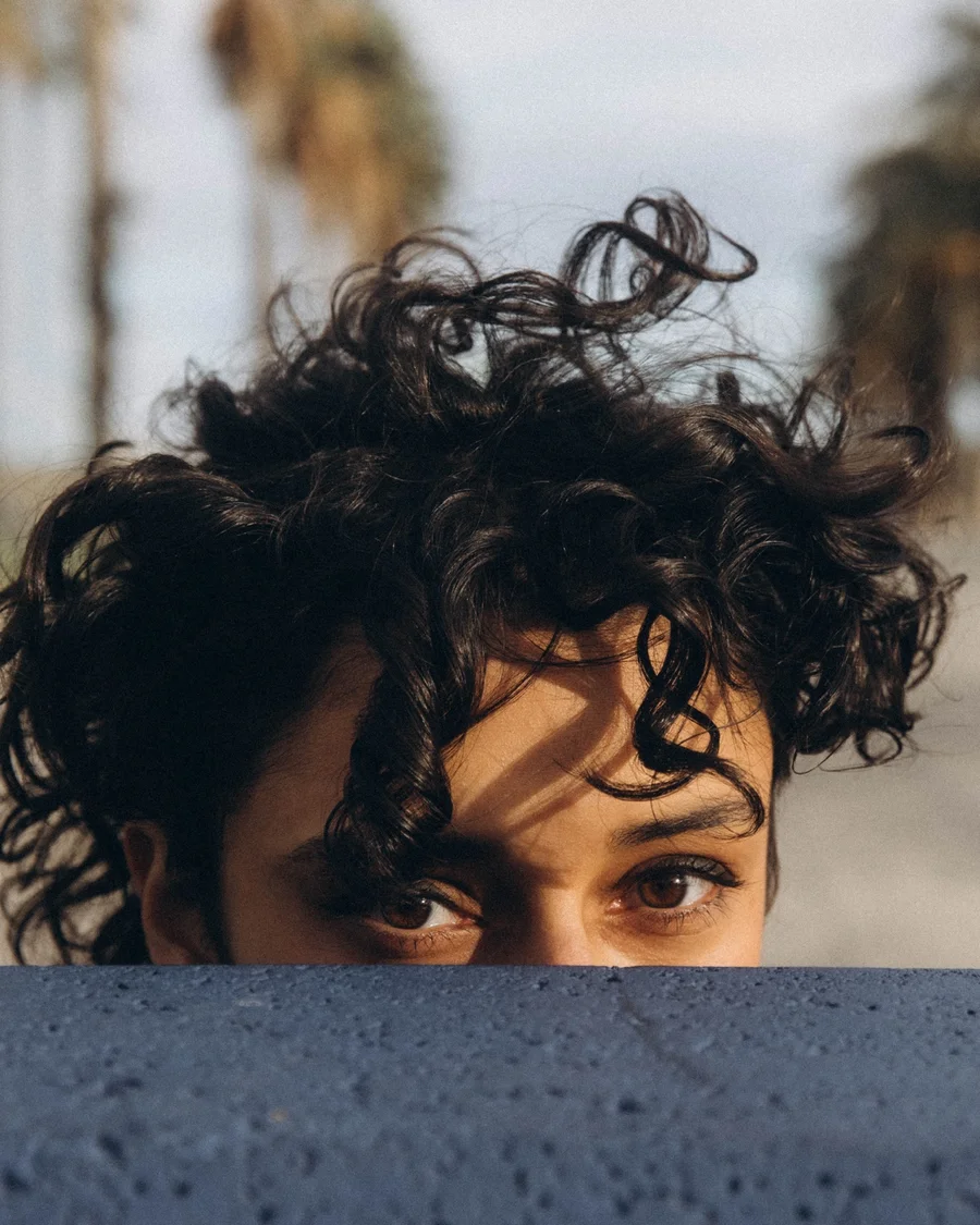 Woman with curly hair looking over a concrete wall